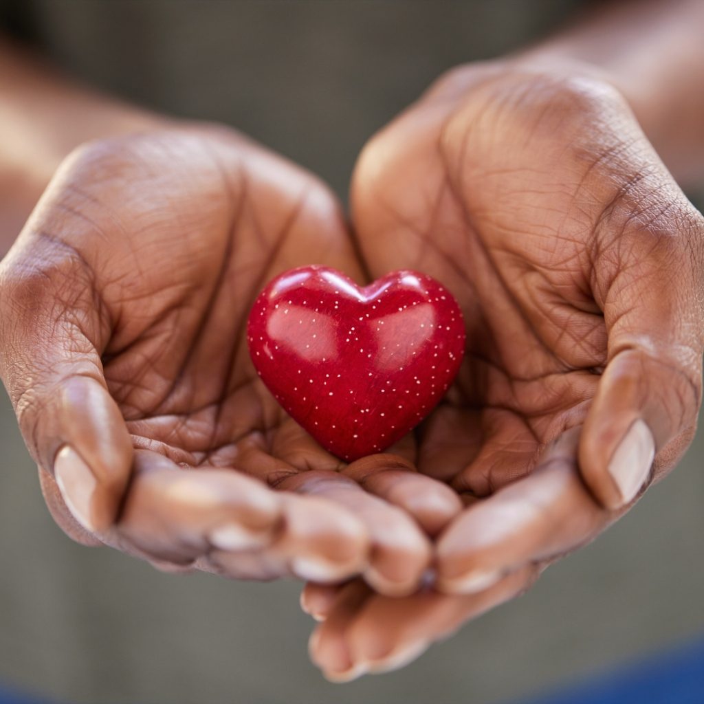 Close up of black woman hands holding a small red heart. Small heart in the hands of a african woman. Solidarity, charity and responsibility concept.